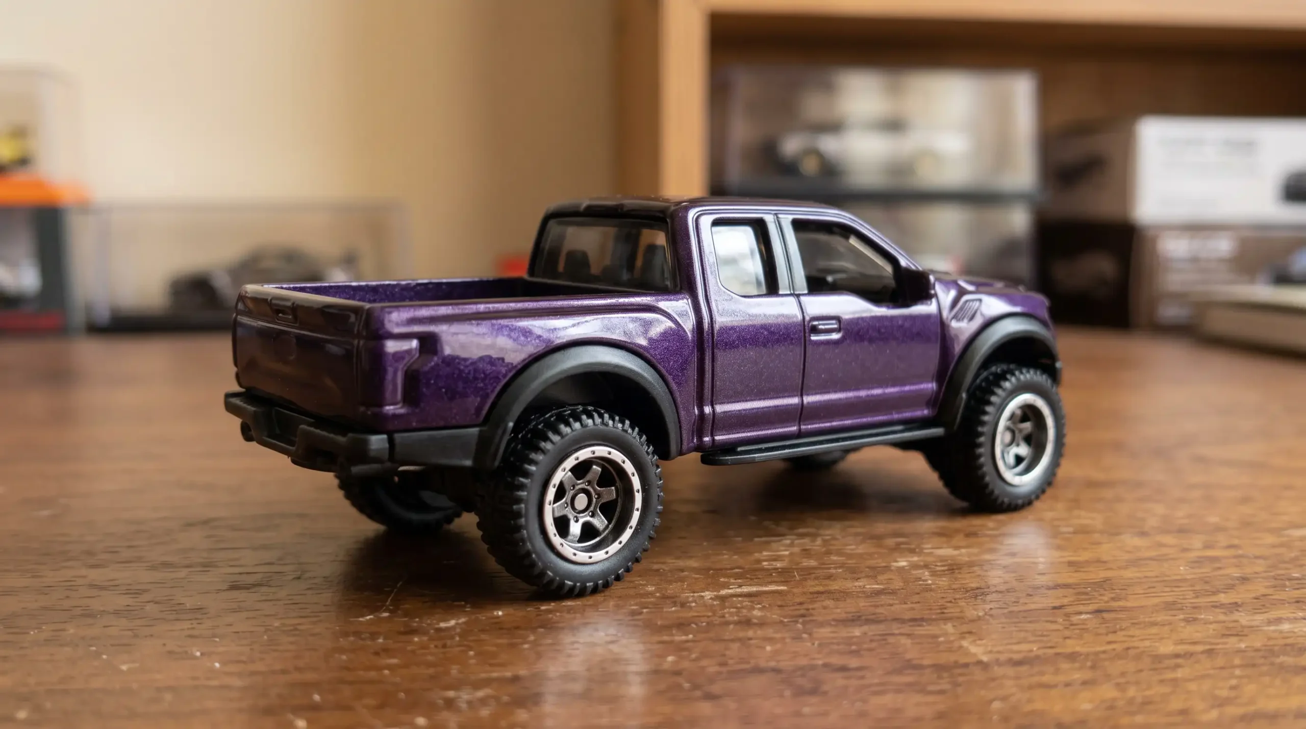 Macro photograph-style image of a purple miniature pickup showing metallic paint, wheels and off-road tire detail.